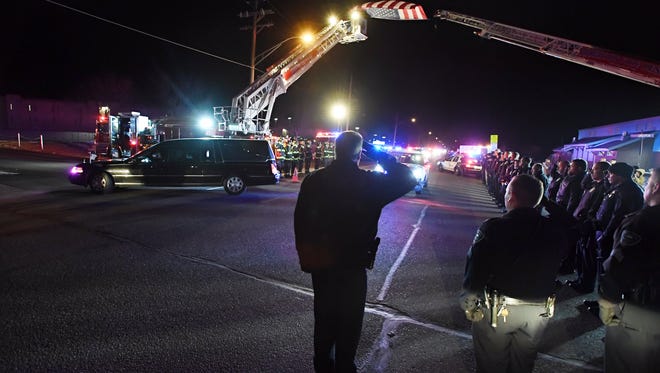 A flag hung down from Truck 53 and Tower 51 to form the archway as Brighton, Colo., police officers stood at attention and saluted as the hearse carrying Adams County Sheriff's Office Deputy Heath Gumm arrives at the Adams county coroner on Thursday, Jan. 25, 2018, in Brighton. Gumm was killed Wednesday night responding to a call in a residential area north of downtown Denver, the sheriff's office said. (John Leyba/The Denver Post via AP)