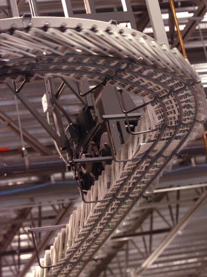 Newspapers travel along an overhead conveyer belt, each being held by an individual gripper, while being transported from the printing press to a packaging station.
