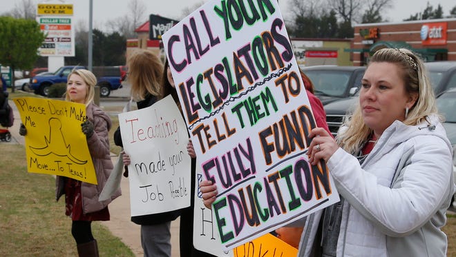 In this Tuesday, March 27, 2018, photo, teacher Adrien Gates pickets with other educators on a street corner in Norman, Okla.