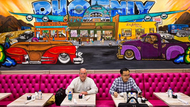 Roger Sorochty (left)  of Tulsa, Okla., and Harry Yoo of Gilbert  enjoy a bite to eat beneath a mural at the Barrio Cafe in Terminal 4 at Phoenix Sky Harbor International Airport.