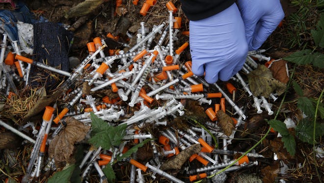 In this Nov. 8, 2017, file photo, a volunteer cleans up needles used for drug injection that were found at a homeless encampment in Everett, Wash.