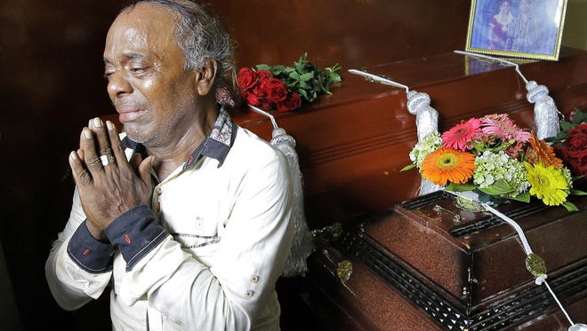 Baby Joseph Gomes prays standing next to coffins of his family members killed in the Easter Sunday bombings in Colombo, Sri Lanka, Tuesday, April 23, 2019. Gomes lost five members of his family.