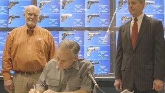 Texas Gov. Greg Abbott (center) signs a bill lowering fees for handgun licenses with the measure's authors, state Sen. Robert Nichols, left, and Rep. Phil King on May 26, 2017.