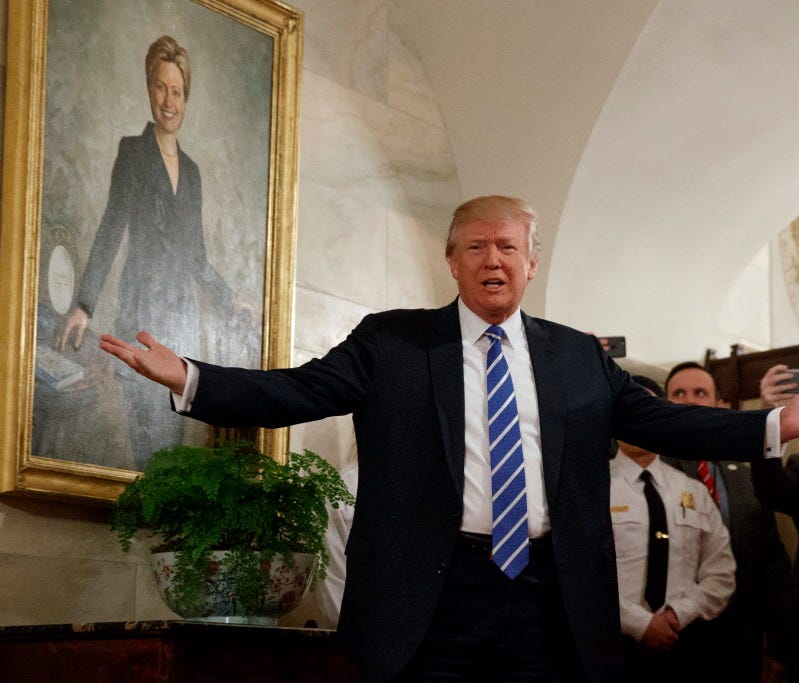 President Trump at the White House in front of a Hillary Clinton portrait.