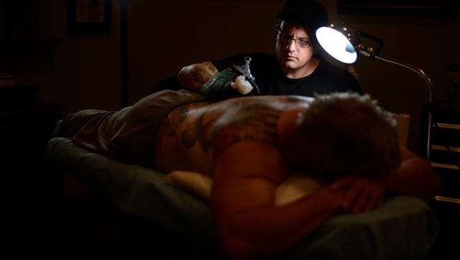 Tattoo artist Paul Dhuey is highlighted by a lamp as he works on John Utrie's back piece inside his studio Katana Tattoo in Green Bay on Wednesday, Aug. 21, 2013. The back piece is a turtle vs. snake with Japanese maple leave. Evan Siegle/Press-Gazette Media