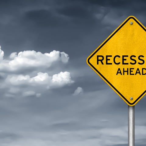 A yellow street sign says recession ahead, with bl
