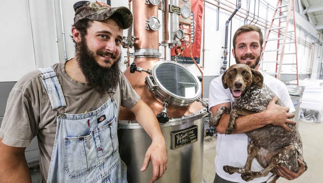 Co Founders of the 8th Day Distillery, Mason Laming, left, and Matt Lamping, right, pose for a photo with Dottie the dog in front of "Gertie", their still named after the brothers great grandmother, at their production facility located inside the Circle City Industrial Complex, Thursday September 1st, 2016. The duo picked up their still on their great grandmothers birthday and named it in honor of her.