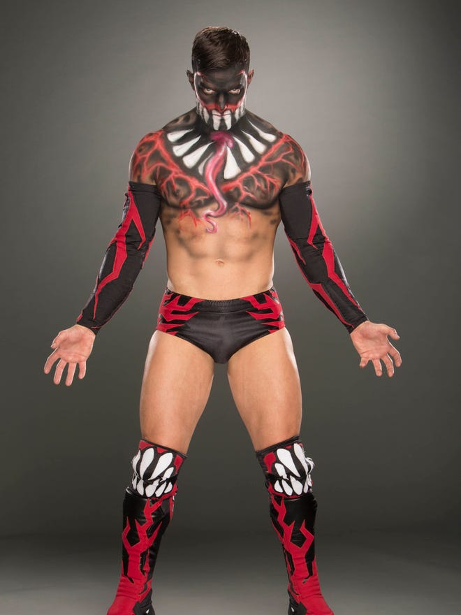 Finn Balor wearing black, venom-monster-like face and upper body paint with red and black trunks, and boots.