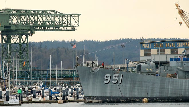 Workers walk Monday along the bow of the USS Turner Joy as the Puget Sound Naval Shipyard looms in the background in Bremerton.