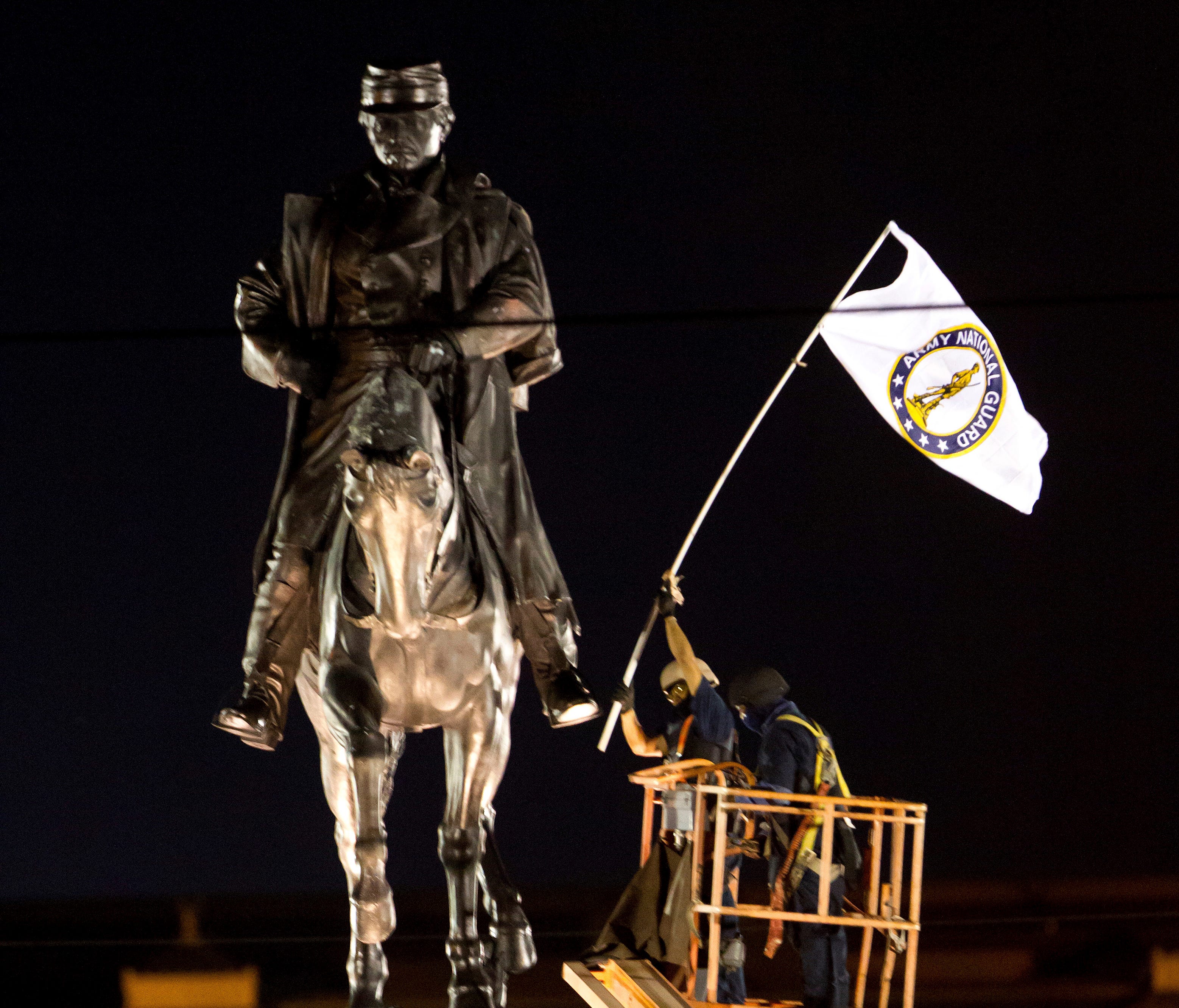 A worker in protective gear takes down an Army National Guard flag from the statue of Confederate General P.G.T. Beauregard during the statue's removal from the entrance to City Park in New Orleans, Tuesday, May 16, 2017.