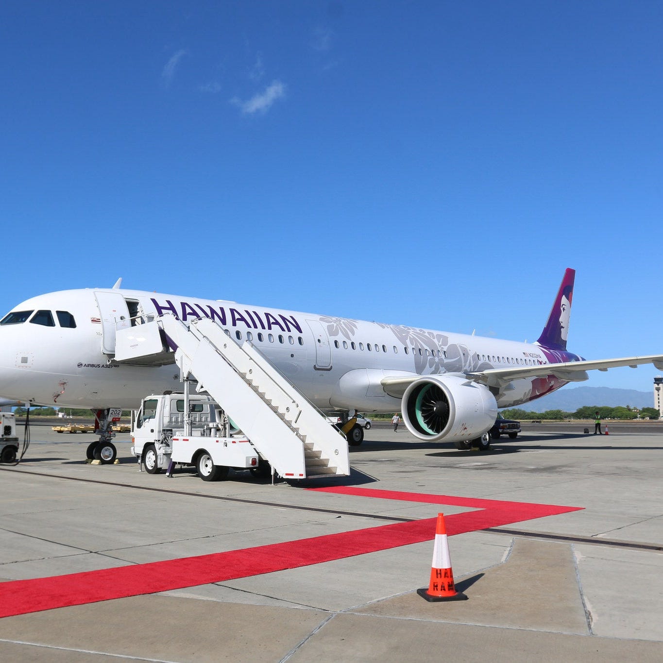 A Hawaiian Airlines plane parked on the ground, with air stairs attached.