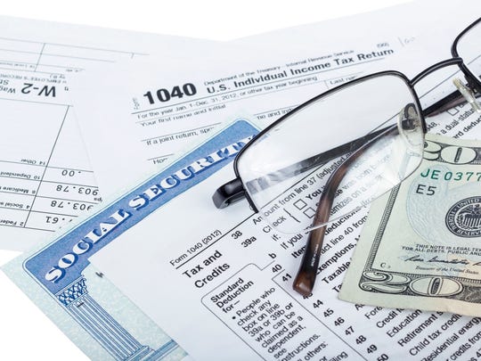 A social security card wedged between the IRS tax forms, with a pair of glasses and a twenty dollar bill lying at the top of the forms.