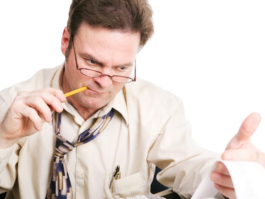 An accountant chewing on a pencil as he closely examines figures from his printing calculator.