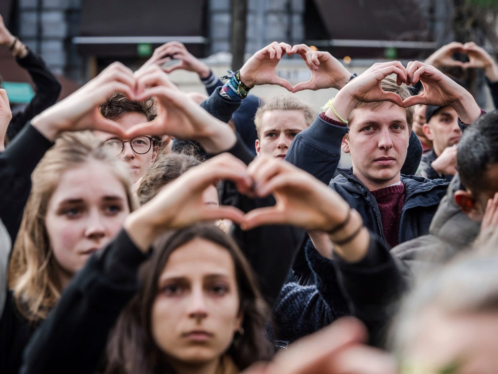 People make the shape of a heart with their hands as they stand for a moment of silence at the Bourse during the one-year anniversary for Brussels attacks victims in Brussels.