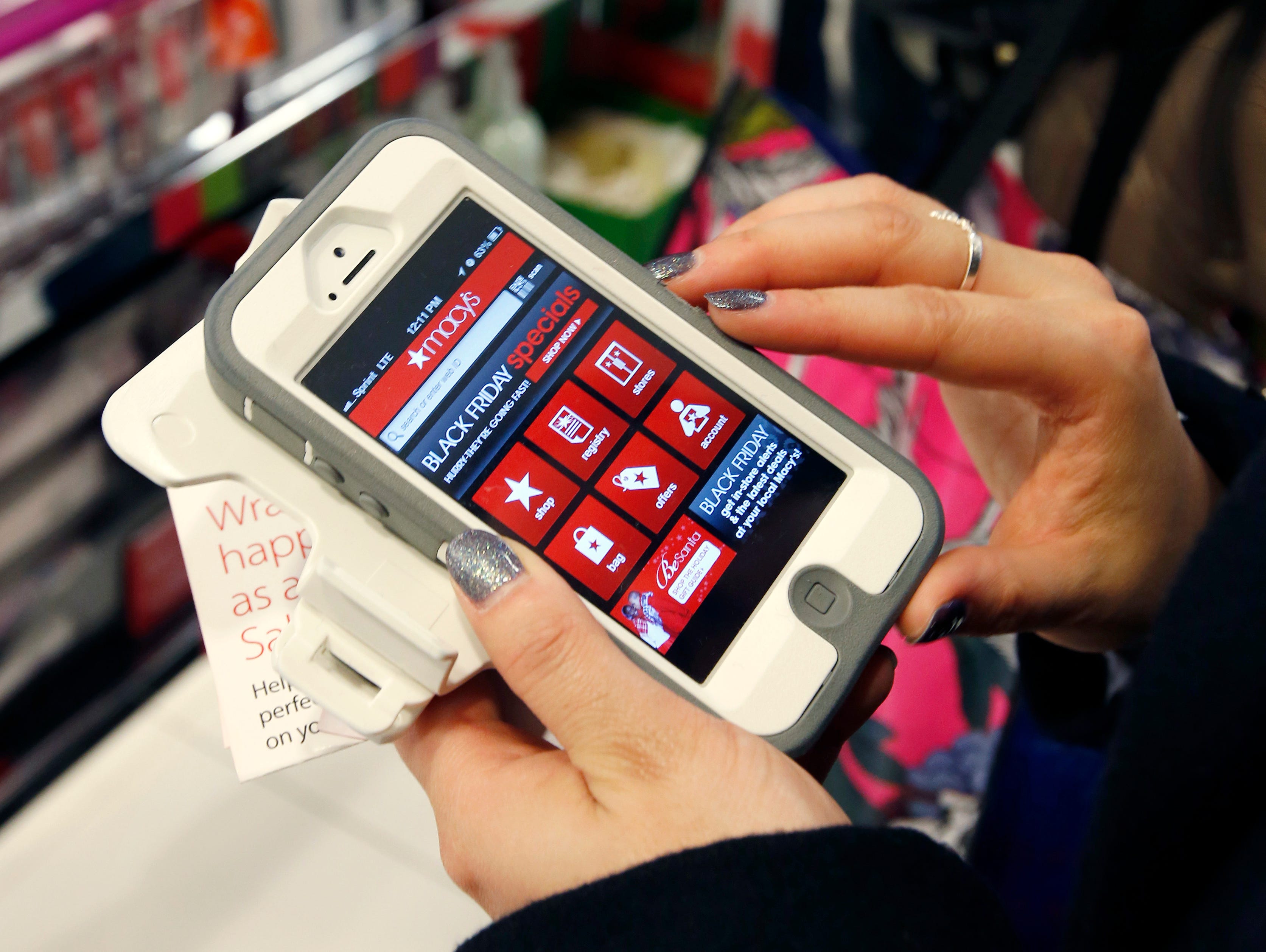 In this Friday, Nov. 23, 2012, file photo, Tashalee Rodriguez, of Boston, uses a smartphone app while shopping at Macy's in downtown Boston. Shoppers are flocking online Monday, Nov. 28, 2016, as 