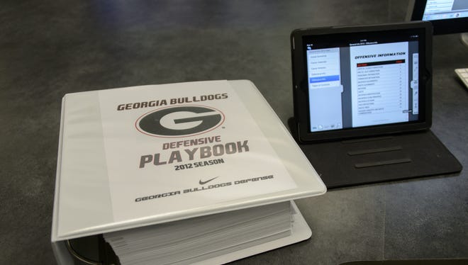 A physical playbook for the Georgia Bulldogs, compared to an iPad, which can hold the contents of the playbook and also show game and practice films.