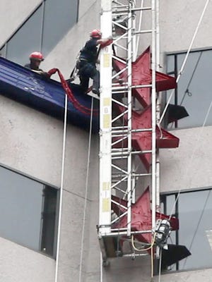 A Cincinnati firefighter climbs from a dangling platform to a roof after the platform broke loose from its anchors on US Bank Tower Tuesday afternoon. No one was hurt.