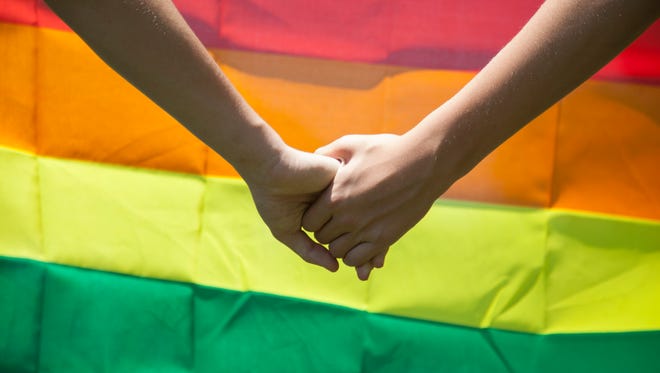 A couple holds hands in front of the Pride Flag.