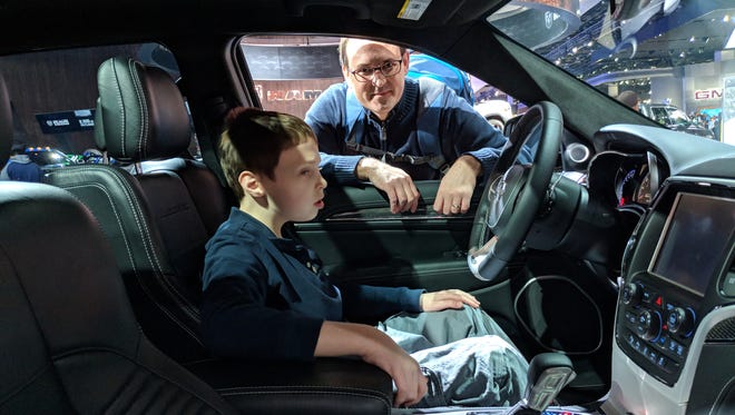 Oliver Hanawalt of Birmingham sits in the driver's seat of a truck at the Detroit Auto Show while his father, Ted, looks on.