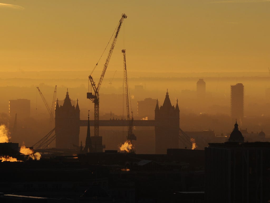 Construction cranes near the Tower Bridge in London at sunrise.