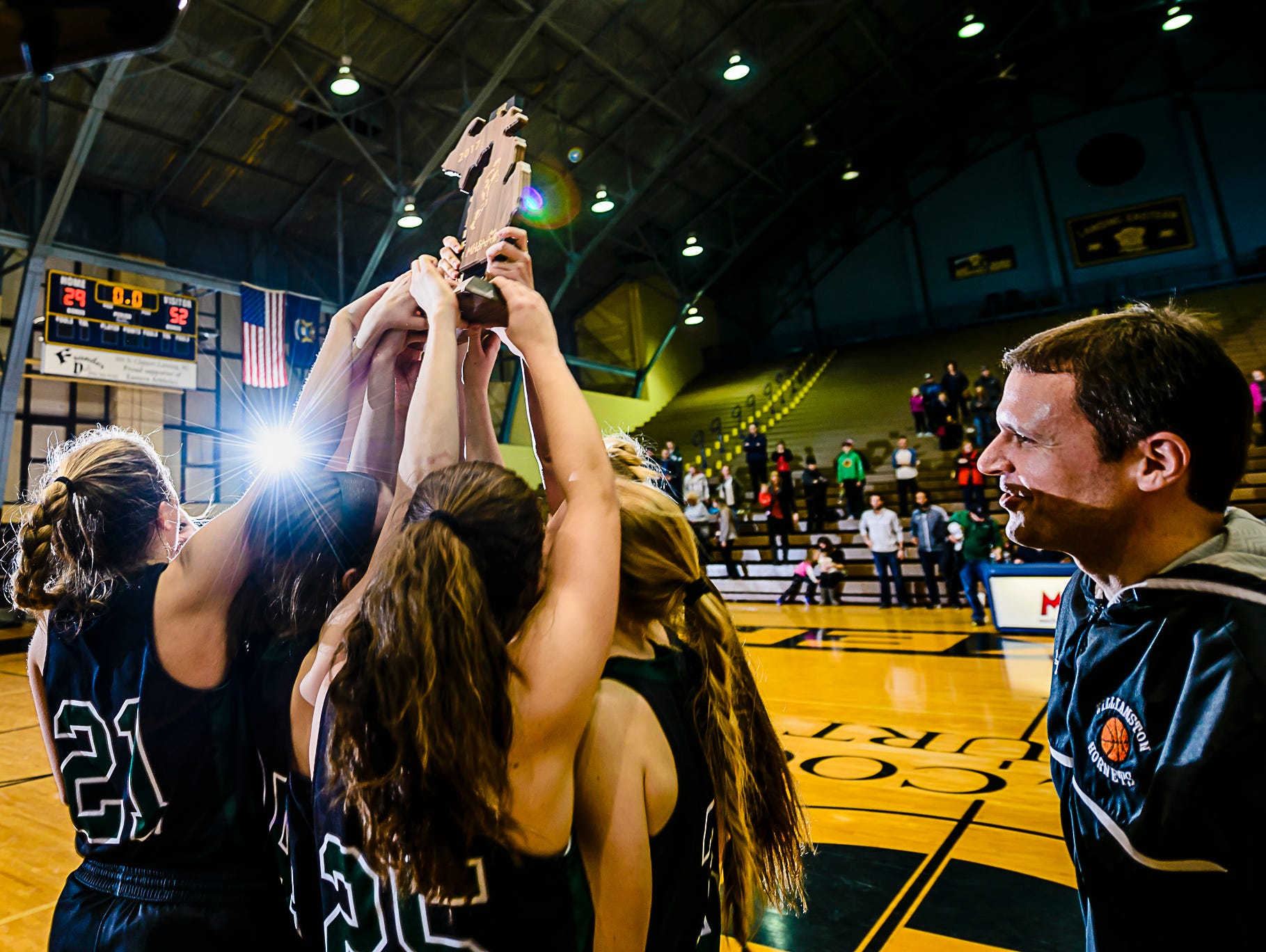 The Williamston girls basketball team lifts the Class B regional championship trophy as head coach Pete Cool ,right, looks on after their win over Portland Thursday March 9, 2017 at Don Johnson Fieldhouse in Lansing. KEVIN W. FOWLER PHOTO