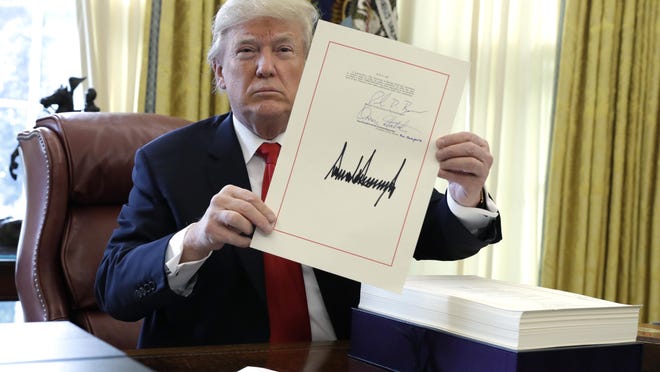 President Donald Trump displays the $1.5 trillion tax overhaul package he signed on Friday in the Oval Office of the White House.