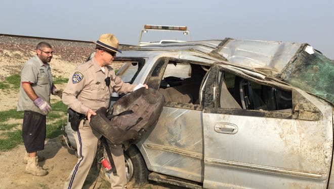 A CHP officer pulls a child's seat out of Ford SUV that crashed Tuesday on Highway 43 at Avenue 16. Five children were in the back seats and two adults in the front. Two children were ejected.