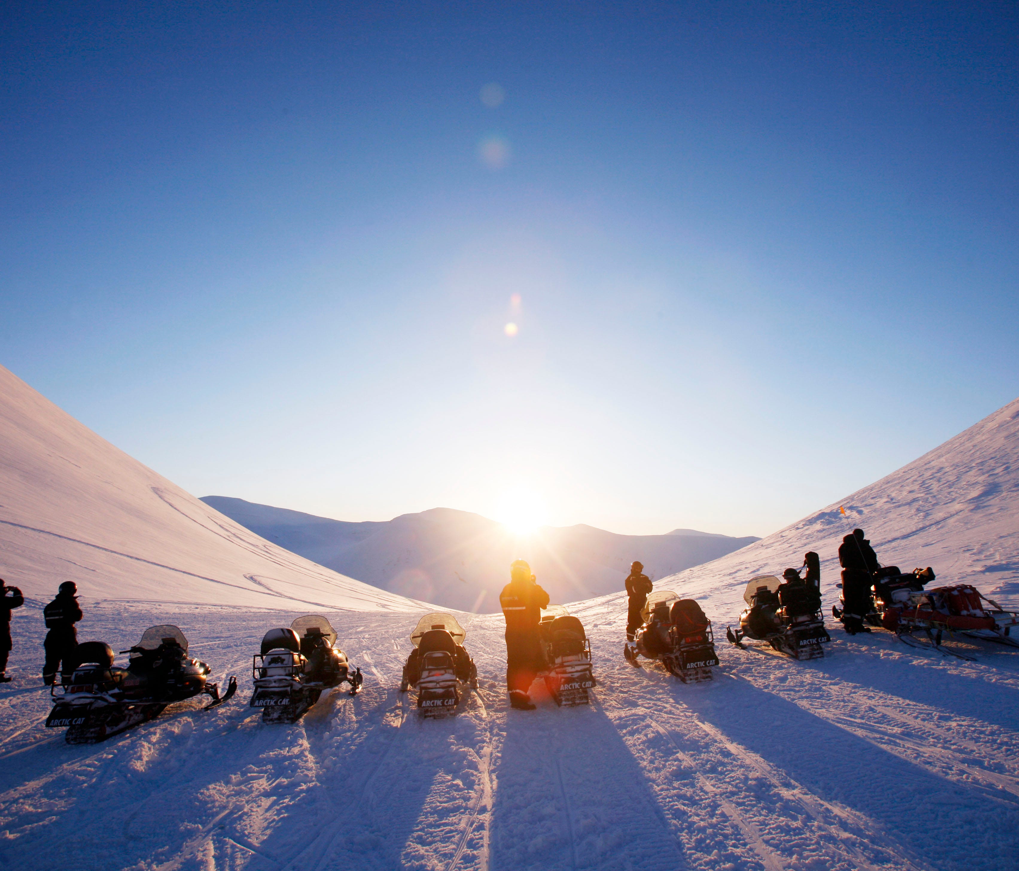 A snowmobile tour makes its way over a glacier toward Barentsburg, Norway.