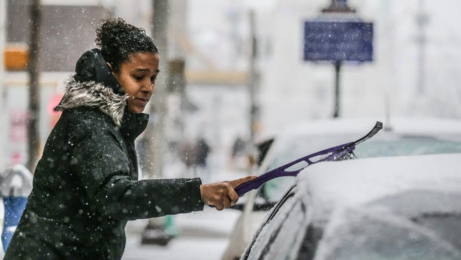 Nicole Woodson brushes off her car as snow falls in Indianapolis on Friday, Dec. 29, 2017. 