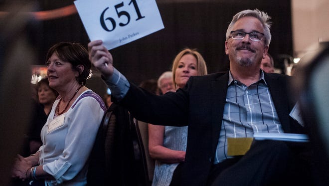 John Parkes of Bozeman holds up his bid number after winning "Summer Evening on the Missouri" by Jeff Walker during The Russell Live Auction in the Mansfield Center.
