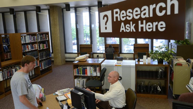 Matt Van Ess, seated, the department coordinator for research, local history and genealogy, helps a patron at the reference desk of the Brown County Central Library in downtown Green Bay.