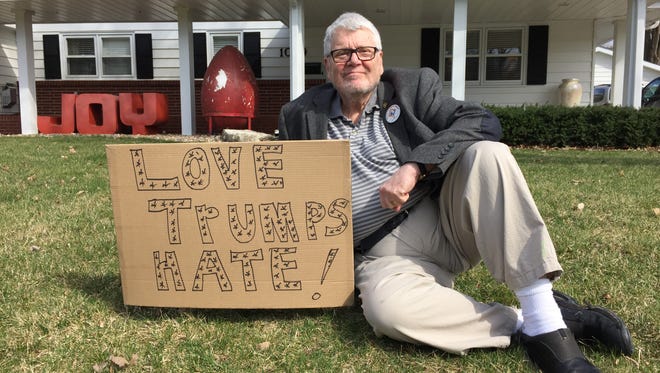 The Rev. Milton Cole-Duvall of West Des Moines sits in his front yard next to the sign he posted a week ago in response to this divisive political year in America.
