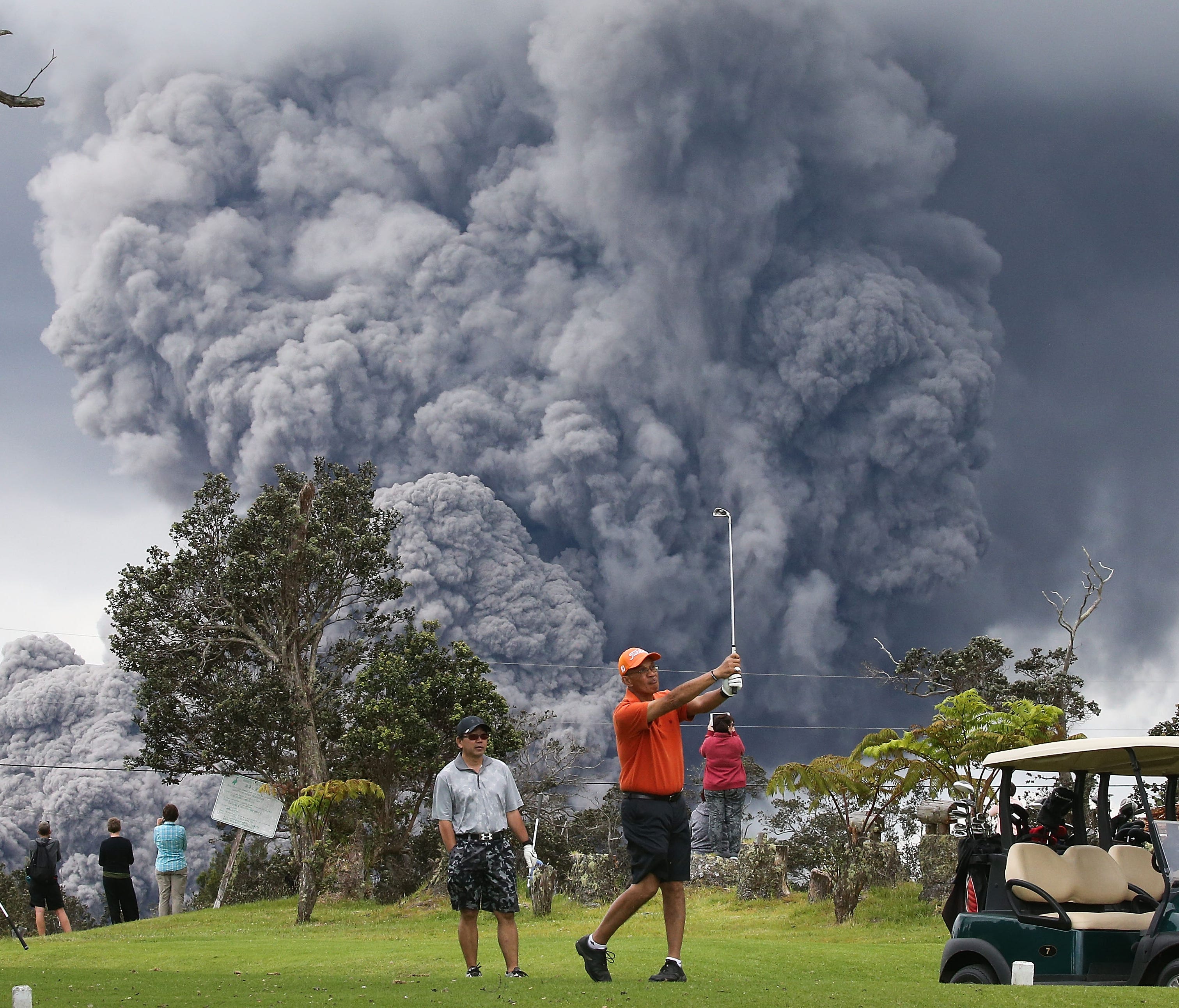  People play golf as an ash plume rises in the distance from the Kilauea volcano on Hawaii's Big Island May 15, 2018 in Hawaii Volcanoes National Park, Hawaii.