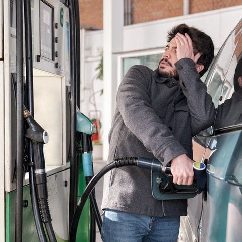 A young adult refuels their car while looking worr