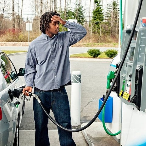 A young adult pumps gas with a concerned expressio