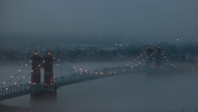 Fog hugs the Ohio River as it passes under the Roebling Suspension Bridge.