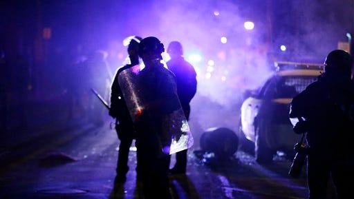 FILE - In this Nov. 25, 2014 file photo, police officers watch protesters as smoke fills the streets in Ferguson, Mo. after a grand jury's decision in the fatal shooting of Michael Brown. A Justice Department investigation has found patterns of racial bias in the Ferguson police department and at the municipal jail and court. The full report, to be publicly released on March 4, says the investigation found Ferguson officers disproportionately used excessive force against blacks and too often charged them with petty offenses. (AP Photo/Charlie Riedel, File)