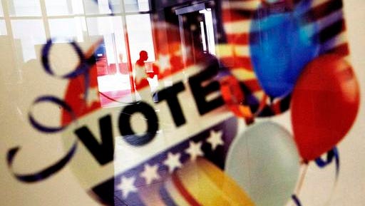 In this Nov. 1, 2016, photo, a voter is reflected in the glass frame of a poster while leaving a polling site in Atlanta, during early voting ahead of the Nov. 8 election day. If all goes smoothly, the American people will choose a new president on Tuesday, the Electoral College will affirm the election and either Democrat Hillary Clinton or Republican Donald Trump will take the oath of office Jan. 20.