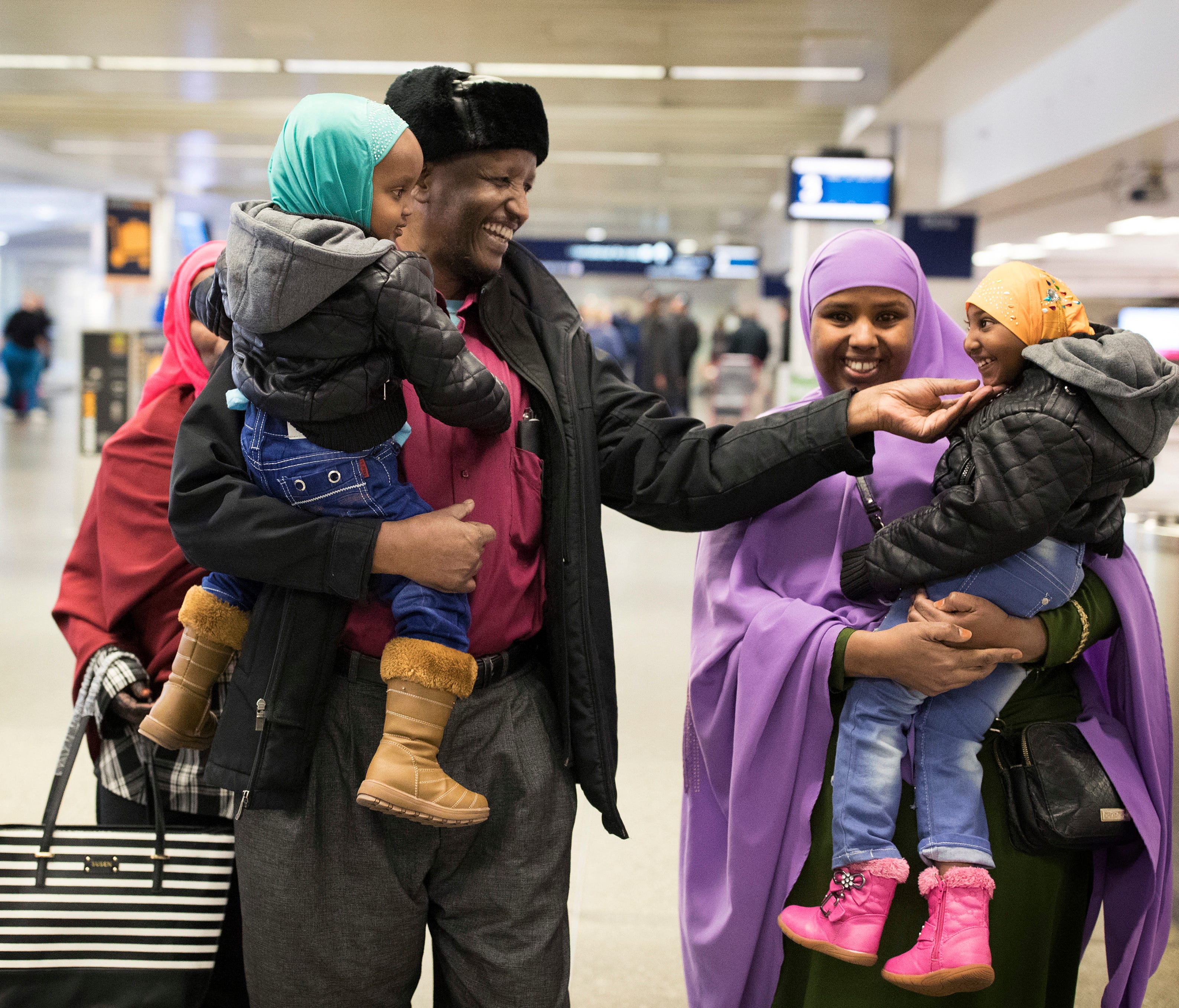 Mohamed lye, carrying his 2-year-old daughter, Nafiso, plays with his 4-year-old daughter, Nimo, carried by family friend Abdinasir Abdulahi, at Minneapolis–Saint Paul International Airport near Bloomington, Minn., after arriving from Amsterdam on  F