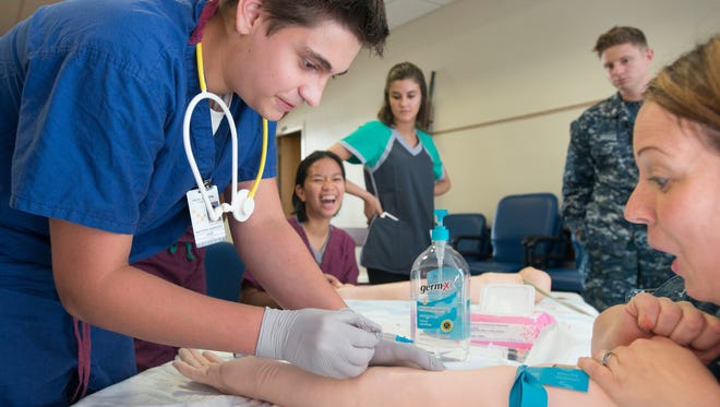 Matthew Hamricks of Tate High School, left, gets set to start an IV during the Summer Medical Preparatory Program at the Navy Hospital in Pensacola.
