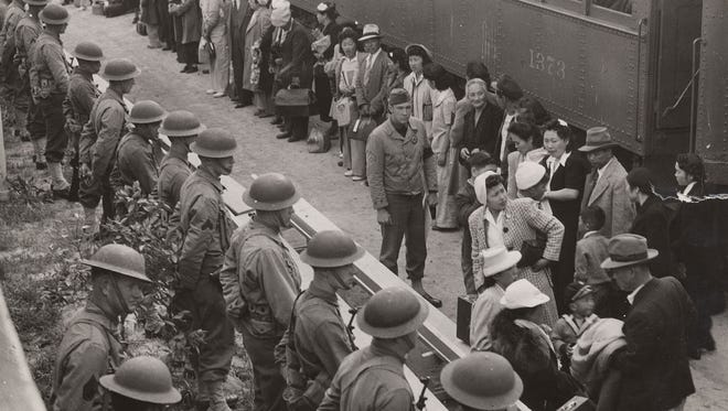 第二次世界大戦中、米国政府は12万人の日系人を強制収容所に強制収容しました。 この写真では、警備員が日本人の男性、女性、子供たちが捕虜収容所に連れて行く電車に乗るのを待っているのを見ています。