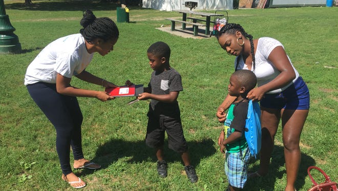 Satara Brown, founder of Rebuilding Our Children and Community, left, hands a notebook and folder to Christian Brown, 7, of the City of Poughkeepsie, while his mother, Leniece Jones, helps her other son, Xavier, 5, with a backpack. Free school supplies were distributed Saturday in Waryas Park.