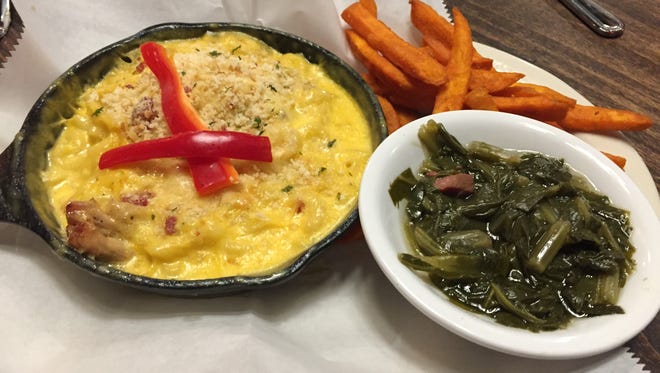Piggy Mac is cherry wood-smoked pulled pork in an iron skillet, topped with smoked Gouda macaroni and cheese, served with sweet potato fries and turnip greens at Puckett's Grocery.