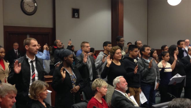 A group of new American citizens raise their right hands as they swear an oath of citizenship.