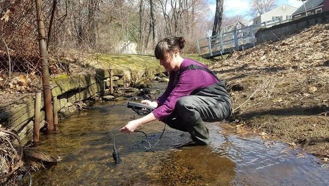 Mara Tippett, RHA well test manager, using a sensor for chemical monitoring of a stream