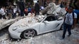 A man stands next to a car crashed by debris from a