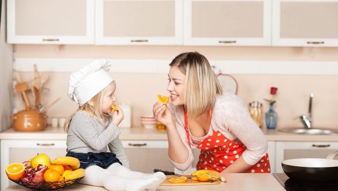Little cute girl with her mother eating orange while cooking. Kitchen interior. Concept for young kitchen hands