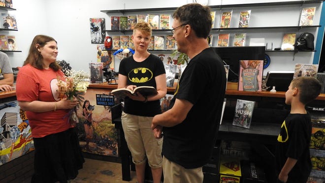 Standing on flood-damaged flooring, Black Ice Comics owner Shana Porteen, center, performs the wedding ceremony for Melanie and Clint Salmi as best man Peyton Salmi looks on at the Houghton, Mich., comic-book store Wednesday, July 4, 2018. The groom wore a Batman shirt while the bride chose the Flash. Clint and Melanie Salmi are giving marriage a second try with help from the Upper Peninsula comic book shop.