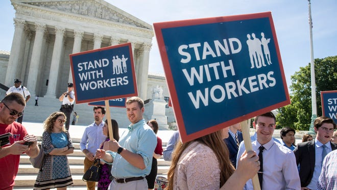 In this Monday, June 25, 2018 photo, people gather at the Supreme Court awaiting a decision in an Illinois union dues case, Janus vs. AFSCME, in Washington.  The Supreme Court says government workers can't be forced to contribute to labor unions that represent them in collective bargaining, dealing a serious financial blow to organized labor.