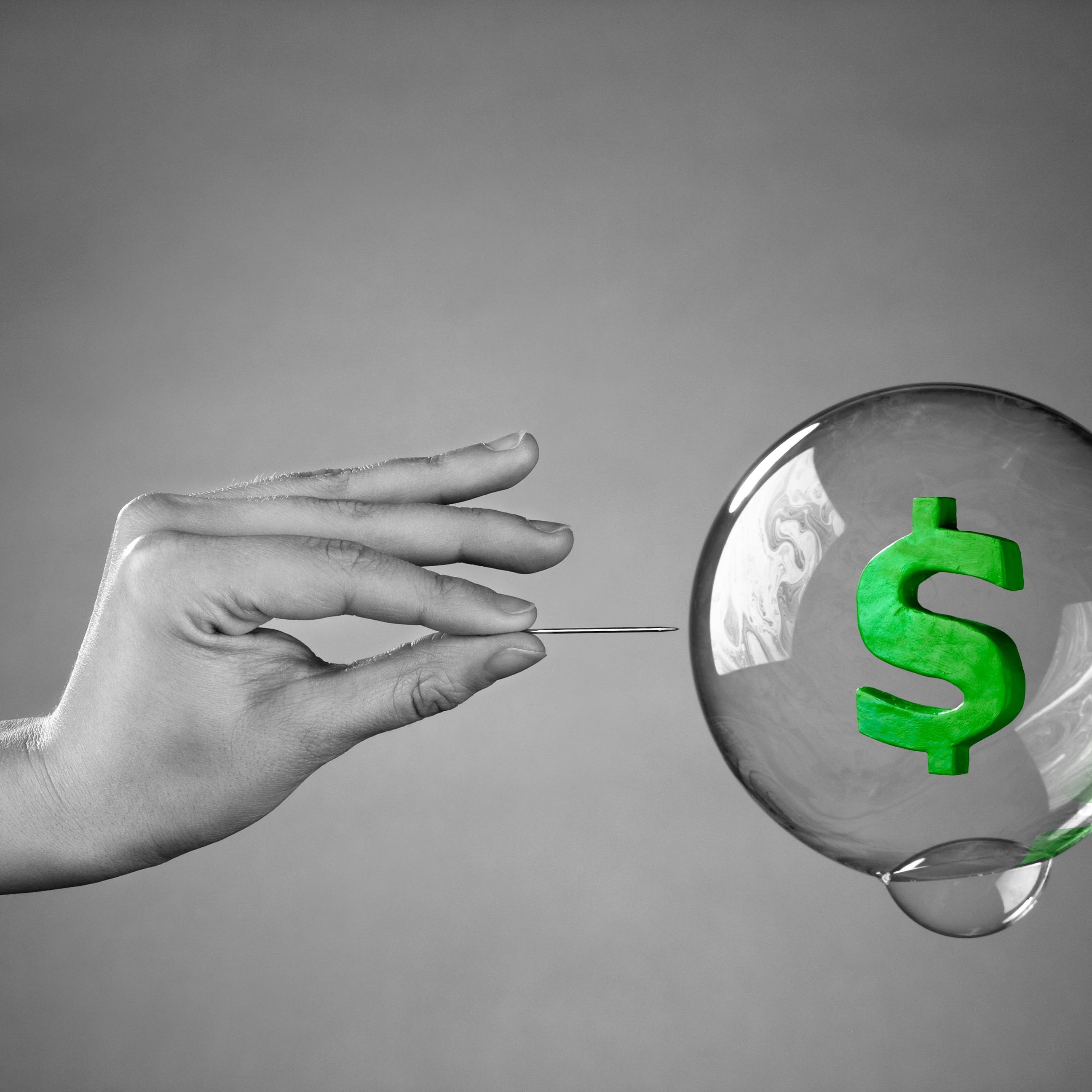 A soap bubble with a dollar sign in it about to be popped by a hand holding a pin.